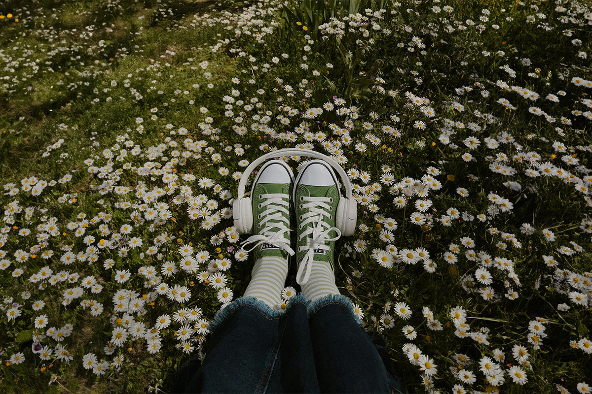 feet with vans shoes and headset in a field of daisies